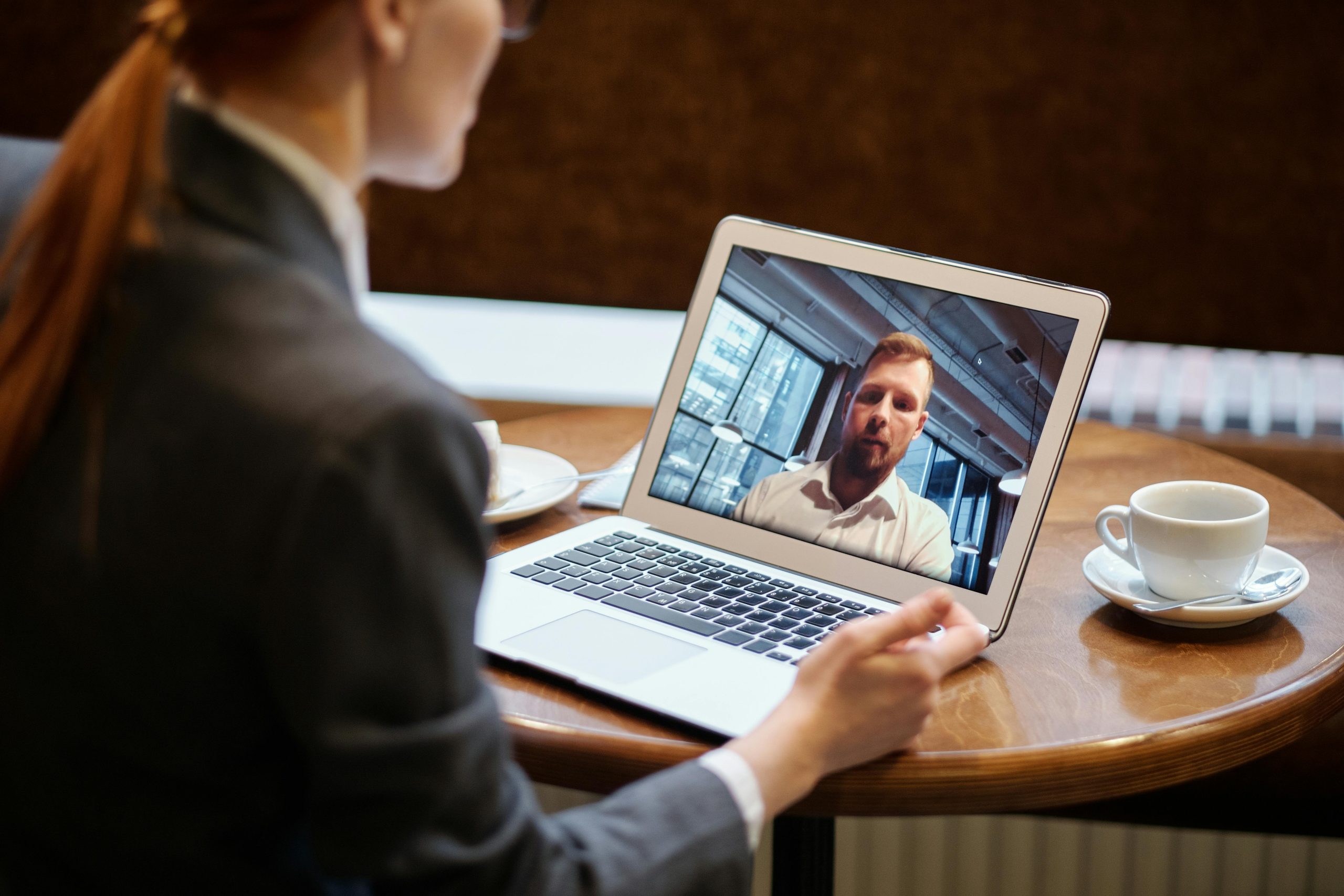 Woman connecting with a man in a video call on a laptop placed on a coffee shop table